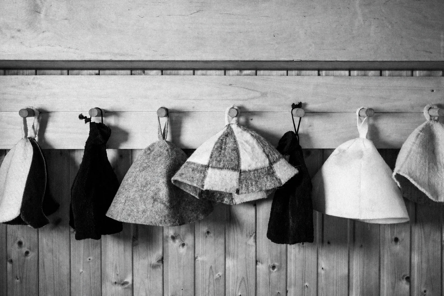 Black-and-white photograph of sauna hats hanging on a wooden wall
